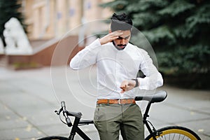 Smart and confident indian businessman looking at his watch while late to meet by bicycle, copy space