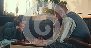 Smart cute teen girl makes move playing chess with old senior grandfather at home. Intelligence and logical thinking.