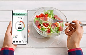 Man eating vegetable salad and counting calories on mobile application