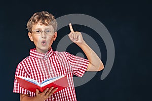 Smart, enthusiastic boy with glasses and a book in his hand, pointing up