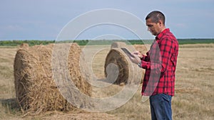 Smart farming agriculture concept lifestyle. Man worker farmer studying a haystack in a field on digital tablet. Slow