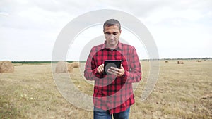 Smart farming agriculture lifestyle concept. man farmer studying a haystack in a field on digital tablet. slow motion