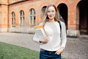 Smart female college student with bag and books on campus outdoors
