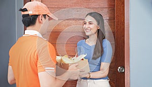 Smart food delivery service man in orange uniform handing fresh food to recipient and young woman customer receiving order from co