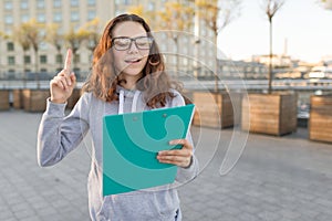 Smart girl with glasses looking at the clip-board and showing index finger up