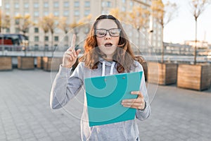 Smart girl with glasses looking at the clip-board and showing index finger up attention, idea, eureka, golden hour
