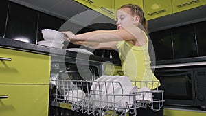 Smart girl learning to use dishwasher. Stylish modern Built In Kitchen Appliances in green black. Child is putting clean