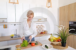 Smart girl slices cucumber with knife and smiles, standing at ki