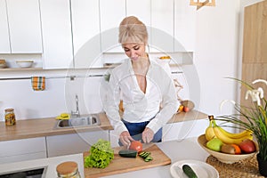 Smart girl slices cucumber with knife and smiles, standing at ki