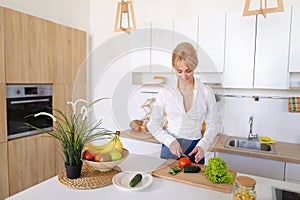 Smart girl slices cucumber with knife and smiles, standing at ki