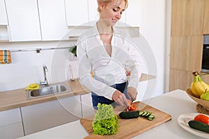 Smart girl slices cucumber with knife and smiles, standing at ki