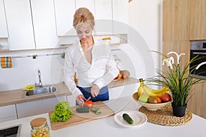 Smart girl slices cucumber with knife and smiles, standing at ki