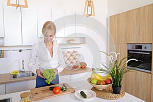 Smart girl slices cucumber with knife and smiles, standing at ki