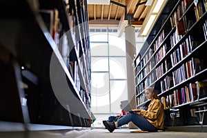 Smart girl student using laptop sitting in university library on floor.