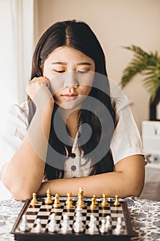 Smart girl teen thinking while playing Chess boardgame at home for training her brain and memory