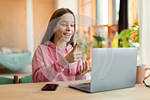 Smart girl teenager having video conference with teacher from home, using laptop and talking at webcamera