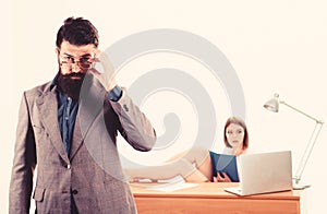 Smart and good looking guy. Smart man looking through glasses with sexy woman working in background. Bearded man in