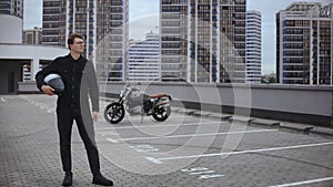 Smart guy stands in front of motorbike with helmet at top of multi-level parking