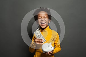 Smart happy black child boy putting in piggy bank one dollars banknote