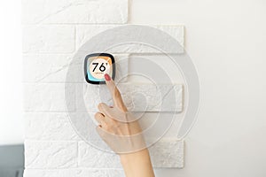 Smart home digital thermostat touch screen woman touching touchscreen to adjust temperature of heating in living room