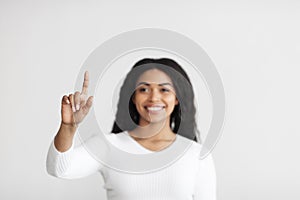 Smart home. Young african american lady pointing finger in the air pushing button on invisible screen