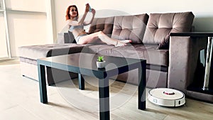 Smart House. Cleaning the house`s robotic vacuum cleaner, when women based on sofas play mobile phones