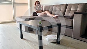 Smart House. Cleaning the house`s robotic vacuum cleaner, when women based on sofas play mobile phones