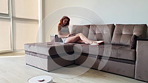 Smart House. Cleaning the house`s robotic vacuum cleaner, when women based on sofas play mobile phones