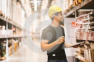 Smart Indian engineer man worker doing stocktaking of product management in cardboard box on shelves in warehouse.