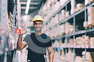 Smart Indian engineer man worker wearing safety helmet doing stocktaking of product management in cardboard box