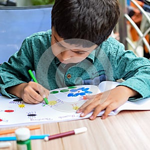 Smart Indian little boy perform thumb painting with different colourful water colour kit during the summer vacations, Cute Indian