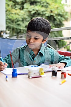 Smart Indian little boy perform thumb painting with different colourful water colour kit during the summer vacations, Cute Indian