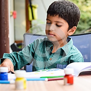 Smart Indian little boy perform thumb painting with different colourful water colour kit during the summer vacations, Cute Indian