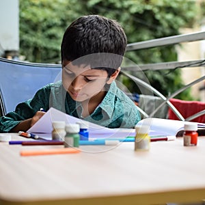 Smart Indian little boy perform thumb painting with different colourful water colour kit during the summer vacations, Cute Indian