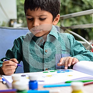 Smart Indian little boy perform thumb painting with different colourful water colour kit during the summer vacations, Cute Indian