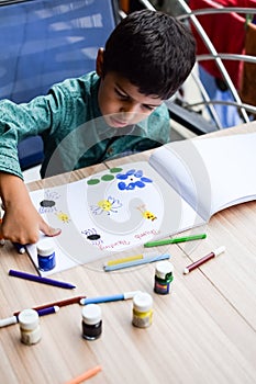 Smart Indian little boy perform thumb painting with different colourful water colour kit during the summer vacations, Cute Indian