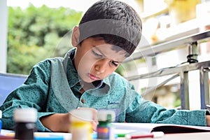 Smart Indian little boy perform thumb painting with different colourful water colour kit during the summer vacations, Cute Indian