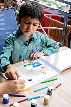 Smart Indian little boy perform thumb painting with different colourful water colour kit during the summer vacations, Cute Indian