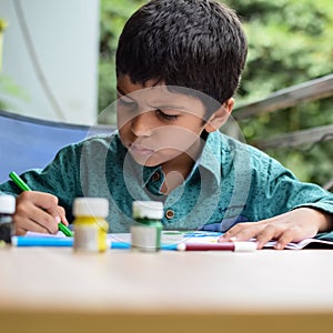 Smart Indian little boy perform thumb painting with different colourful water colour kit during the summer vacations, Cute Indian