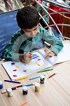 Smart Indian little boy perform thumb painting with different colourful water colour kit during the summer vacations, Cute Indian