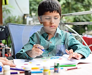 Smart Indian little boy perform thumb painting with different colourful water colour kit during the summer vacations, Cute Indian