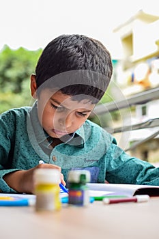 Smart Indian little boy perform thumb painting with different colourful water colour kit during the summer vacations, Cute Indian