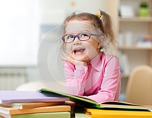 Smart kid girl in eye glasses reading books in her room