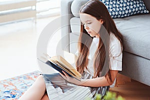 Smart kid girl reading interesting book at home