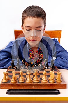 Smart little boy playing chess, a teen grandmaster with vintage chess board