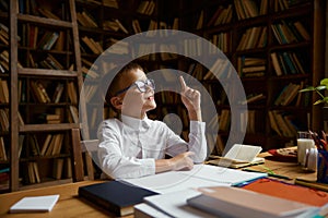 Smart little boy student having idea sitting at table desk in home library