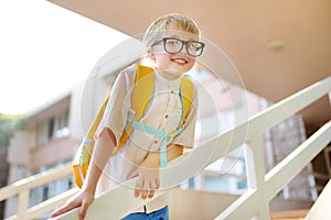 Smart little child with backpack on the stairs of school building. Quality education for children. Portrait of funny nerd