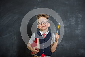 Smart little child boy near blackboard. back to school. Kid in glasses with pencil pointing up.