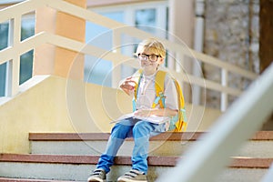 Smart little child sitting and reading on the stairs of school building. Quality education for children. Portrait of funny nerd