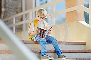 Smart little child sitting and reading on the stairs of school building. Quality education for children. Portrait of funny nerd